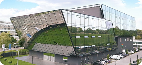 Modernes, futuristisches Bürogebäude mit Glasfassade und abgewinkelter Architektur, umgeben von grünen Rasenflächen.