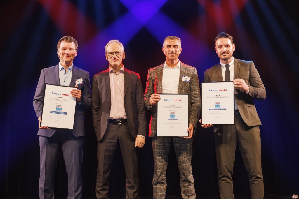 Drei Männer halten Telekom-Preise auf der Bühne, rotes und blaues Licht im Hintergrund.