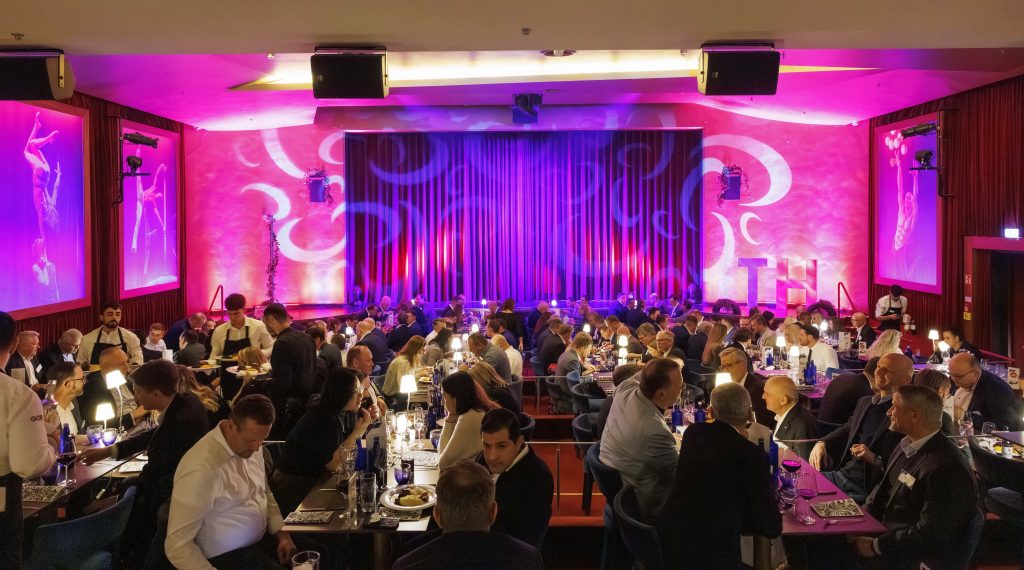 Gäste genießen ein festliches Dinner in einem stimmungsvoll beleuchteten Veranstaltungsraum mit rotem Vorhang.